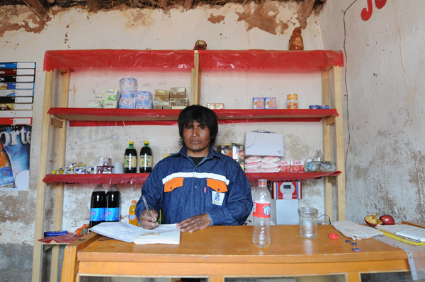 Südamerikanischer Mann steht in einem sparsam ausgestatteten Verkaufskiosk und notiert etwas in ein Buch